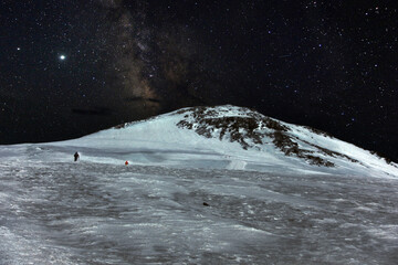 Climbing Elbrus. Snow-capped mountain peaks and figures of climbers at night. The mountains are covered with snow at night.