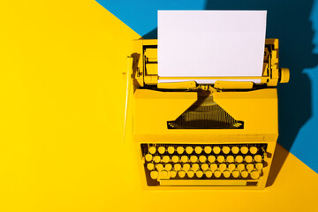 Yellow bright typewriter on a yellow and blue background. Symbol for writing, blogging, new ideas and creativity. Copy space - obrazy, fototapety, plakaty