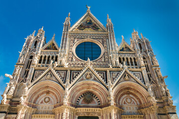 Naklejka premium Idealne zbliżenie z niskiego kąta zachodniej elewacji słynnej Duomo di Siena, średniowiecznej katedry w Sienie we Włoszech. Zbudowany z polichromowanego marmuru, dzieło nadzorował Giovanni Pisano.