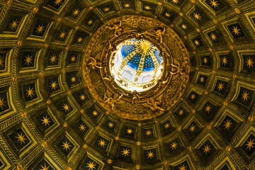 Close-up view of the interior of the Duomo di Siena's hexagonal dome. It is topped with Bernini's gilded lantern, like a golden sun. The trompe l'oeil coffers were painted in blue with golden stars.