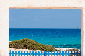 Panoramic view of Formentera island, Spain. Stone portal with a blue wooden fence, in the background the Mediterranean sea, the blue sky, and sailing boats sailing