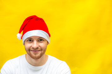 Portrait of a young man in a santa claus hat on a yellow background. New Year 2021. Copy space