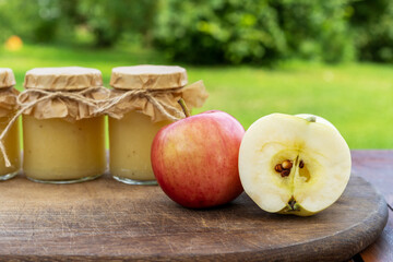 Apple puree jars on the wooden table in blurred green garden background. Freshly prepared organic homemade baby food.