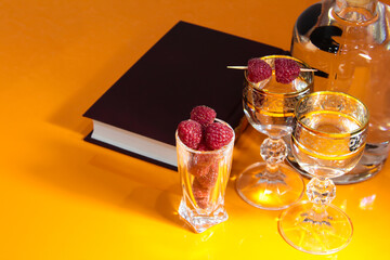Vodka on an orange table with a book and raspberries.