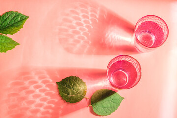 flat lay with glasses with clear water and shadows on pink background