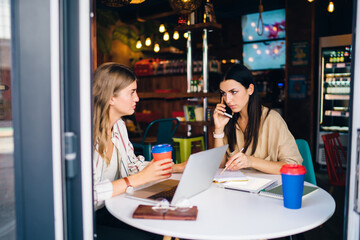 Serious women sitting in modern cafe with gadgets and coffee and working on project