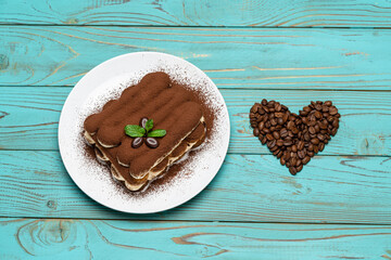 portion of Classic tiramisu dessert on ceramic plate and heart shaped coffee beans on colorful blue wooden background