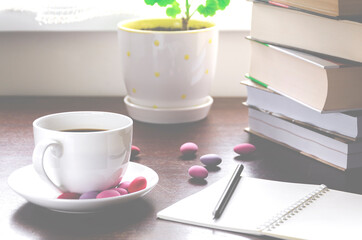 A cozy concept. A cup of coffee with multicolored chocolates stands on a wood table next to a stack of old books