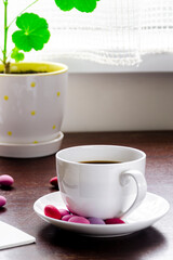 A cozy concept. A cup of coffee with multicolored chocolates stands on a wood table next to a stack of old books