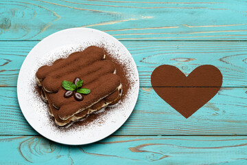 portion of Classic tiramisu dessert on ceramic plate and heart shaped cocoa powder on colorful blue wooden background