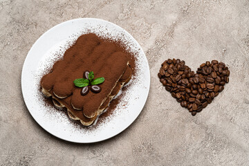 portion of Classic tiramisu dessert on ceramic plate and heart shaped coffee beans on concrete background