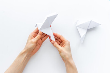Female hands folding sheet of paper - origami bird. Overhead view