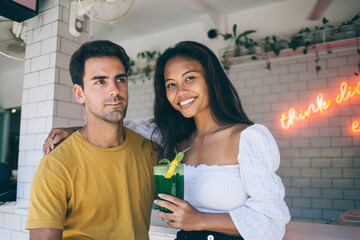 Diverse couple with cocktail hugging in cozy summer cafe