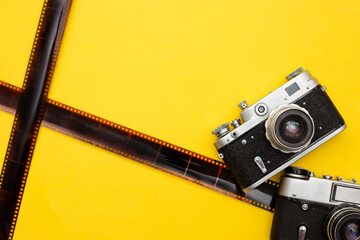 composition with two retro cameras and photographic film on yellow background