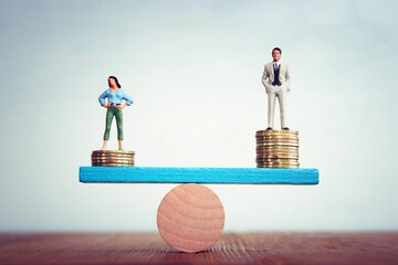 Conceptual image of gender inequality. A woman and a man on either side of the scales, with income...