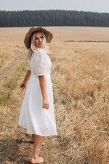 Fototapeta na wymiar A beautiful woman in a white dress and a straw hat walks in the field.