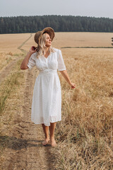 Fototapeta na wymiar A beautiful woman in a white dress and a straw hat walks in the field.