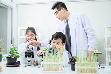 Kids learning about botany hands on. There is a diverse group of children gathered around a microscope and surrounded by plants.