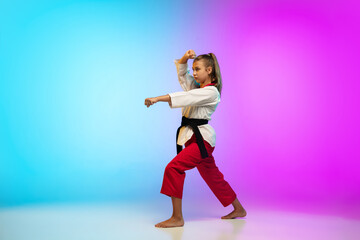 Strong. Karate, taekwondo girl with black belt isolated on gradient background in neon light. Little caucasian model, sport kid training in motion and action. Sport, movement, childhood concept.