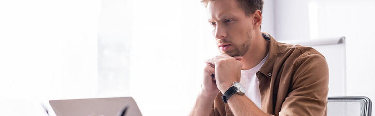 Panoramic shot of young businessman looking at laptop in office