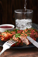 Baked chicken breast with BBQ sausage, parsley and glass of water on a old wooden table and wooden background. Photo with selective focus