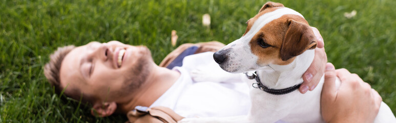 horizontal concept of man lying on lawn with closed eyes and cuddling jack russell terrier dog