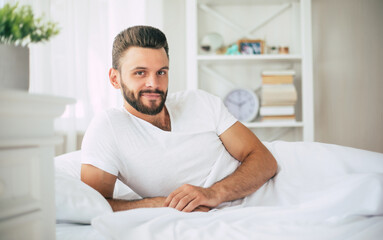 Close up photo of handsome young bearded man lying in bed and relaxing on the morning