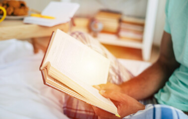 Close up photo of a young guy in pajamas while he reading a book.