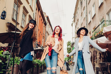 Three young women walking on city street laughing. Girls friends dancing and having fun in Lviv outdoors