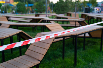 Obraz na płótnie Canvas closed sports playground with wooden benches in a residential area, in a park, near the shopping center and deserted streets are sealed off with a barrier tape that prohibits passage during quarantine