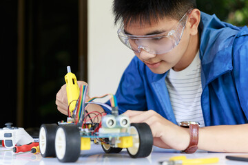 Young asian teen plugging energy and signal cable to sensor chip of toy car workshop.