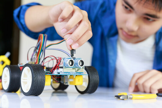 Young asian teen plugging energy and signal cable to sensor chip of toy car workshop.