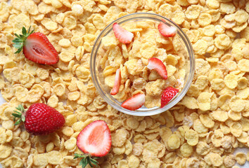 A Cup of cornflakes on a background of flakes with strawberries, top view-the concept of delicious and fast food
