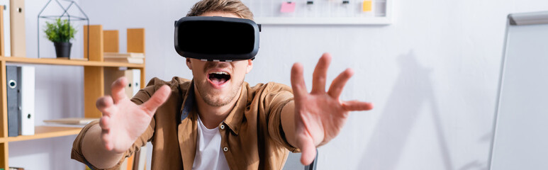 horizontal image of excited businessman gesturing while using vr headset in office