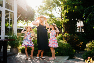 a pregnant mother with two daughters in straw hats and dresses in the backyard garden at sunset. happy single mom with many children. mother's day.