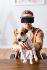 selective focus of young businessman in vr headset holding jack rassell terrier dog in office