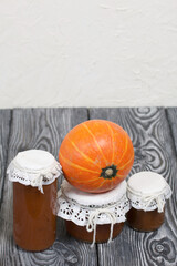 Orange pumpkin and pumpkin jam in jars. On brushed pine boards painted black and white.