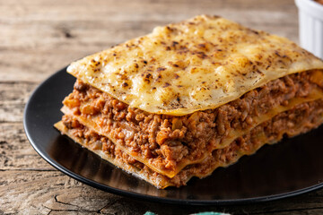 Piece of meat lasagna on black plate on rustic wooden table