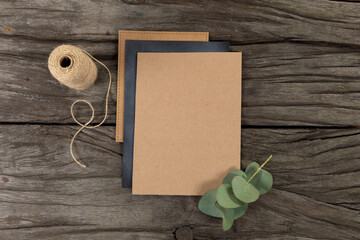 Notebook and black sheet of paper surrounded by a flower and knitting yarn on wood table