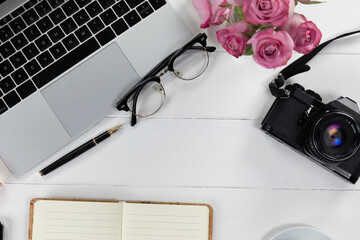 View of a laptop with a camera and glasses, perfume and notebook on white wood table background