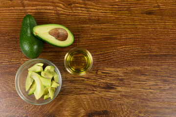 View of two avocados, olive oil bottle and cut avocado in a bowl on wood table background