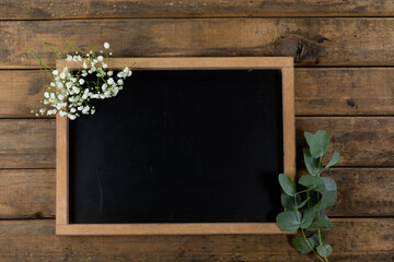 View of a black board surrounded by flowers on wood table background