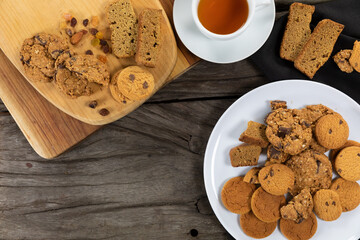 View of some cookies put on a white plate and a wooden cutting board, arranged on on a textured wood
