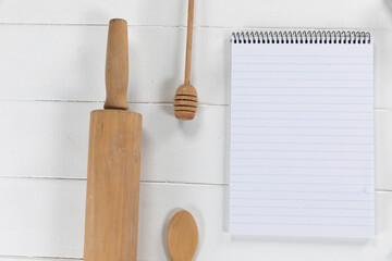 View of a composition with a notebook with wooden spoon and rolling pin on white wooden surface