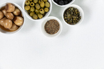 View of a six bowls with fresh tomatoes, olives, nuts and seasoning on plain white surface