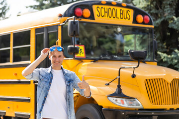 A happy male teacher near school bus