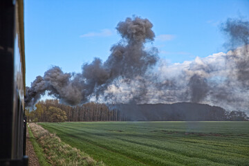 dark smoke from an old coal steam engine over a green field
