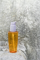 An orange oil bottle next to natural stones against a gray wall with natural light. Trendy style. Cosmetic mockup. Copyspace.