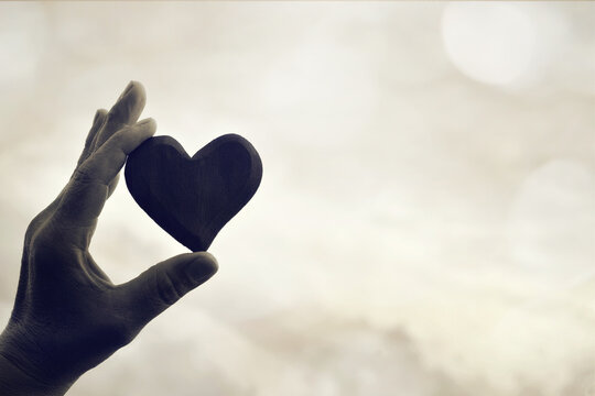 Black and white image of hand holding a heart against sky