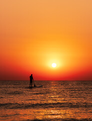 Fototapeta premium Man on the water paddle board at golden sunrise. vertical photo
